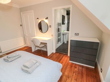 A bedroom with a bed, desk, chair, round mirror, chest of drawers, and an ensuite bathroom at Glenander Bamburgh