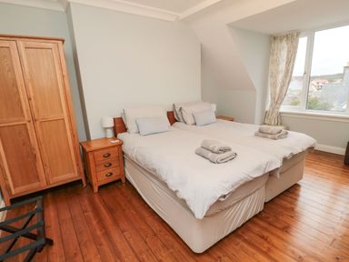 A bedroom with two single beds with towels on them a wooden wardrobe and a window with curtains at Glenander in Bamburgh