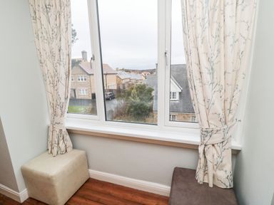 A window with floral curtains with two cushioned seats below it at Glenander in Bamburgh