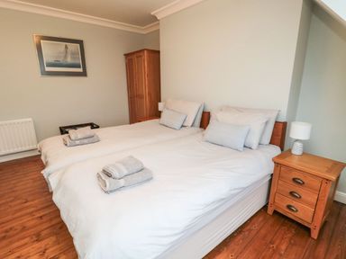 A bedroom with two beds wooden floors and furniture and a painting on the wall at Glenander in Bamburgh