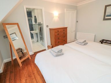 A bedroom with two single beds and folded towels a wooden mirror a chest of drawers and an open door to a bathroom at Glenander Bamburgh
