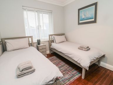 A bedroom with two single beds a nightstand with a lamp and a picture of a sailboat on the wall at Glenander in Bamburgh