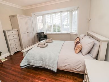 A bedroom with a double bed pillows folded towels a wardrobe a chest of drawers and a black armchair at Glenander in Bamburgh