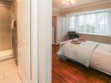 A bedroom with a bed towels on it wardrobe armchair and an adjacent bathroom with a shower at Glenander in Bamburgh