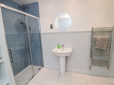 A bathroom with a shower cubicle a sink a round mirror and a towel rack at Glenander in Bamburgh