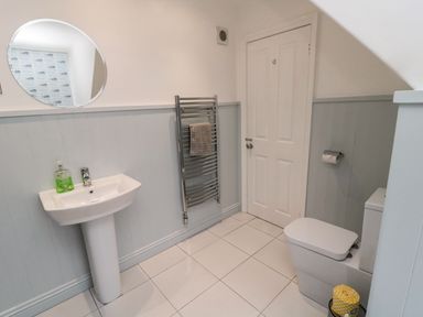A bathroom with a pedestal sink a circular mirror a towel rack a toilet and a door at Glenander in Bamburgh