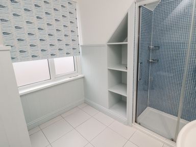 A bathroom with a window with fish patterned blinds shelves under stairs and a shower with blue mosaic tiles at Glenander Bamburgh