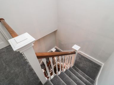 A staircase with grey carpet and wooden handrail at Glenander in Bamburgh