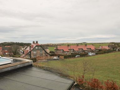 A view of houses with red roofs and green fields in the background at Glenander in Bamburgh