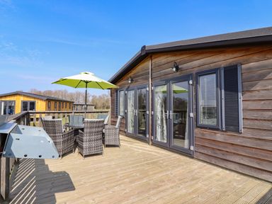 An outdoor wooden deck with a table and wicker chairs under a green umbrella at Skylarks in Fornham St Genevieve near Bury St Edmunds