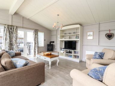 A living room with sofas a coffee table a television and a wood stove at Skylarks in Fornham St Genevieve near Bury St Edmunds