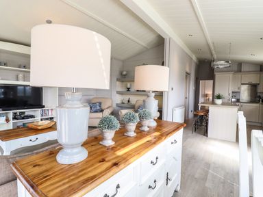 A living room with lamps and plants on a wooden cabinet with kitchen and stools in the background at Skylarks in Fornham St Genevieve near Bury St Edmunds