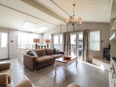 A living room with a brown sofa white coffee table dining table with lamps and plants and glass doors at Skylarks in Fornham St Genevieve near Bury St Edmunds