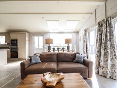 A living room with a brown sofa pillows wooden coffee table table lamps and dining area with plants at Skylarks in Fornham St Genevieve near Bury St Edmunds