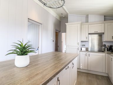 A kitchen with white cabinets a wooden countertop and a potted plant on the island at Skylarks in Fornham St Genevieve near Bury St Edmunds