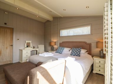 A bedroom with twin beds side by side a brown bench at the foot a dressing table with mirror and chair bedside tables and lamps at Skylarks in Fornham St Genevieve near Bury St Edmunds
