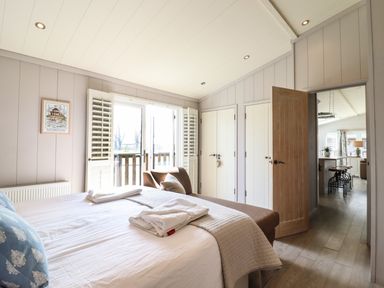 A bedroom with a bed, folded towels, an armchair, closets, and a door leading to a kitchen area at Skylarks in Fornham St Genevieve near Bury St Edmunds