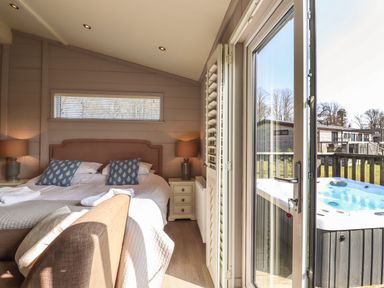 A bedroom with a bed two bedside tables with lamps a sofa and a door leading outside to a hot tub at Skylarks in Fornham St Genevieve near Bury St Edmunds