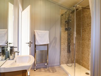 A bathroom with a sink and mirror towel rack with a towel and a glass shower enclosure at Skylarks in Fornham St Genevieve near Bury St Edmunds