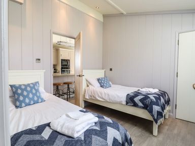 A bedroom with two single beds a door open to a kitchen with bar stools at Skylarks in Fornham St Genevieve near Bury St Edmunds