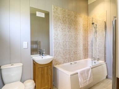 A bathroom with a toilet sink with wooden cabinet mirror bathtub and shower at Skylarks Fornham St Genevieve near Bury St Edmunds