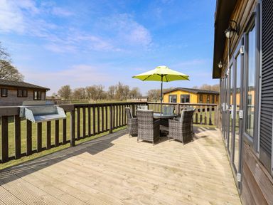 An outdoor wooden deck with a table and four wicker chairs under a green umbrella at Skylarks in Fornham St Genevieve near Bury St Edmunds