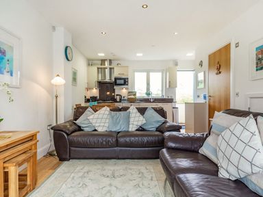 A living room with brown leather sofas and cushions facing a kitchen area with wooden tables at Constantine Bay Cottage in Constantine Bay