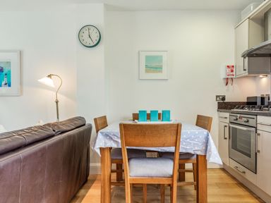 A dining area with a wooden table and chairs next to a kitchen with appliances at Constantine Bay Cottage in Constantine Bay