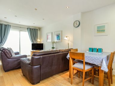 A living room with brown leather sofas a wooden dining table with four chairs and a TV at Constantine Bay Cottage in Constantine Bay