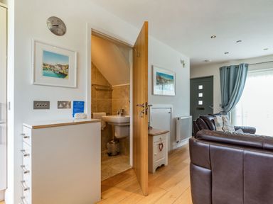 A living room with leather sofas a small cabinet and a partially open door leading to a bathroom at Constantine Bay Cottage in Constantine Bay