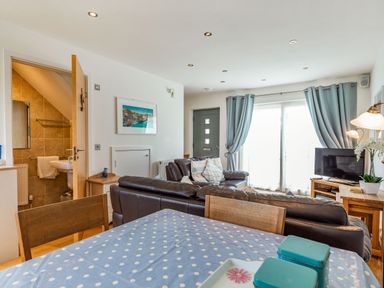 A living room with brown leather sofas a television and blue curtains at Constantine Bay Cottage in Constantine Bay