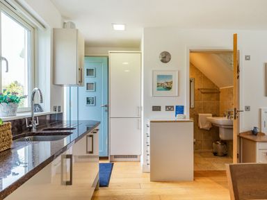 A kitchen with a sink countertop a blue door a white cabinet and an open door to a small bathroom at Constantine Bay Cottage in Constantine Bay