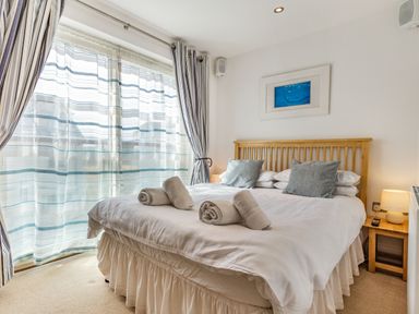 A bedroom with a bed with rolled towels on it next to a window with striped curtains at Constantine Bay Cottage in Constantine Bay