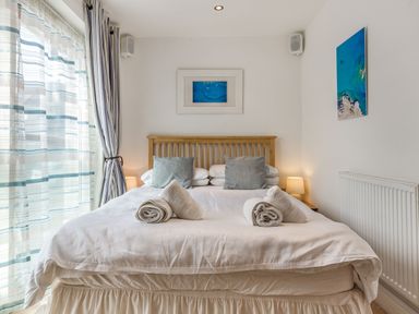 A bedroom with a bed with rolled towels on top bedside tables with lamps and framed pictures on walls at Constantine Bay Cottage in Constantine Bay