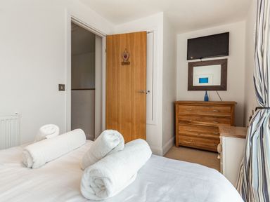 A bedroom with rolled white towels on a bed dresser with a mirror and a television on the wall at Constantine Bay Cottage in Constantine Bay