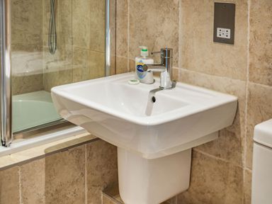 A bathroom sink with soap dispenser and a bar of soap next to a bathtub with glass screen