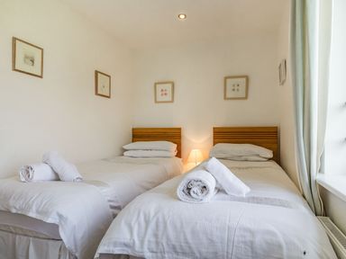 A bedroom with two single beds with white bedding and rolled towels on at Constantine Bay Cottage in Constantine Bay