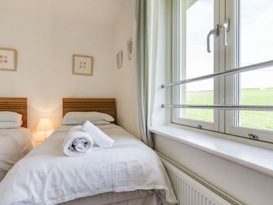 A bedroom with two single beds a lamp and a window showing a field at Constantine Bay Cottage in Constantine Bay