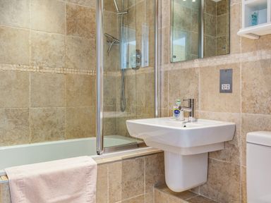 A bathroom with a bathtub shower with glass screen a white sink with hand soap and a towel a toilet at Constantine Bay Cottage in Constantine Bay