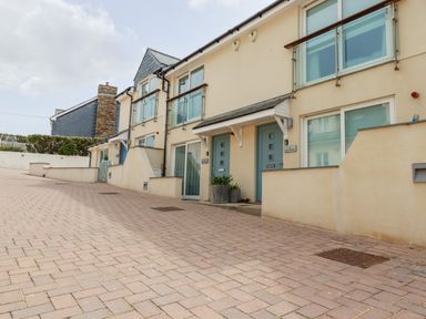 A paved walkway in front of a row of modern two-story houses with blue doors and glass balconies at Constantine Bay Cottage in Constantine Bay