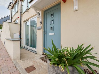 The front entrance of a house with a blue door a large window a plant in a pot and a beige exterior wall at Constantine Bay Cottage in Constantine Bay