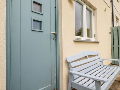 A blue door next to a window and a light blue bench outside a building at Constantine Bay Cottage in Constantine Bay