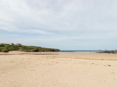 A sandy beach with grassy cliffs and houses in the distance at Constantine Bay
