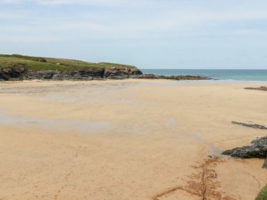 A sandy beach with rocky cliffs and green grass in the background at Constantine Bay Cottage in Constantine Bay