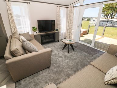 A living room with two beige sofas a round coffee table a TV on a stand and sliding glass doors to a deck at Puffin Lodge in Broad Haven
