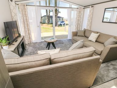 A living room with two sofas a small round table a television and sliding glass doors at Puffin Lodge in Broad Haven