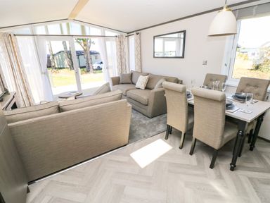 An open living and dining area with two sofas a dining table set for four and large windows at Puffin Lodge in Broad Haven