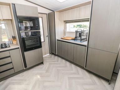A kitchen with built in oven and microwave a window above counter and cabinets at Puffin Lodge in Broad Haven