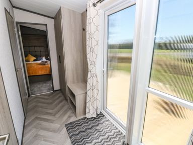 A hallway with wooden storage units leading to a bedroom with a bed and pillows at Puffin Lodge in Broad Haven