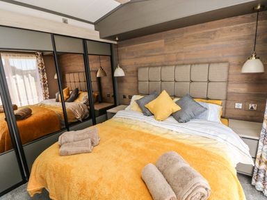 A bedroom with a double bed yellow bedding and towels on the bed beside mirrored wardrobes at Puffin Lodge in Broad Haven